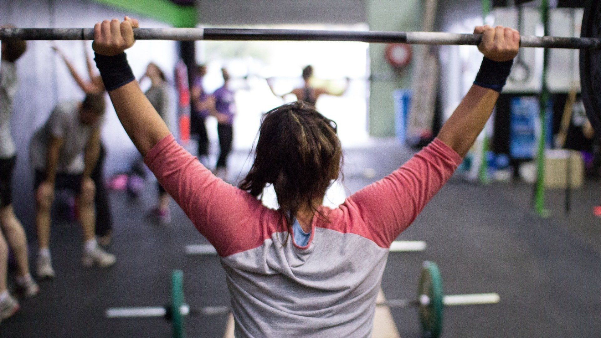 A woman is lifting a barbell over her head in a gym.