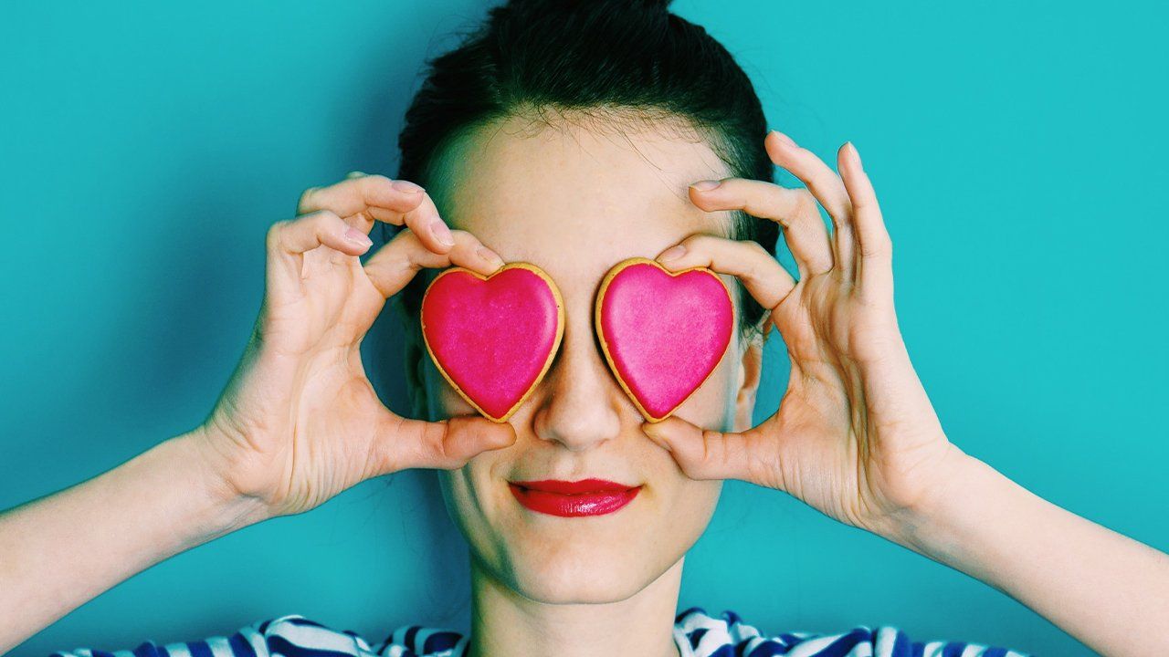 A woman is holding a heart shaped cookie in front of her eyes.