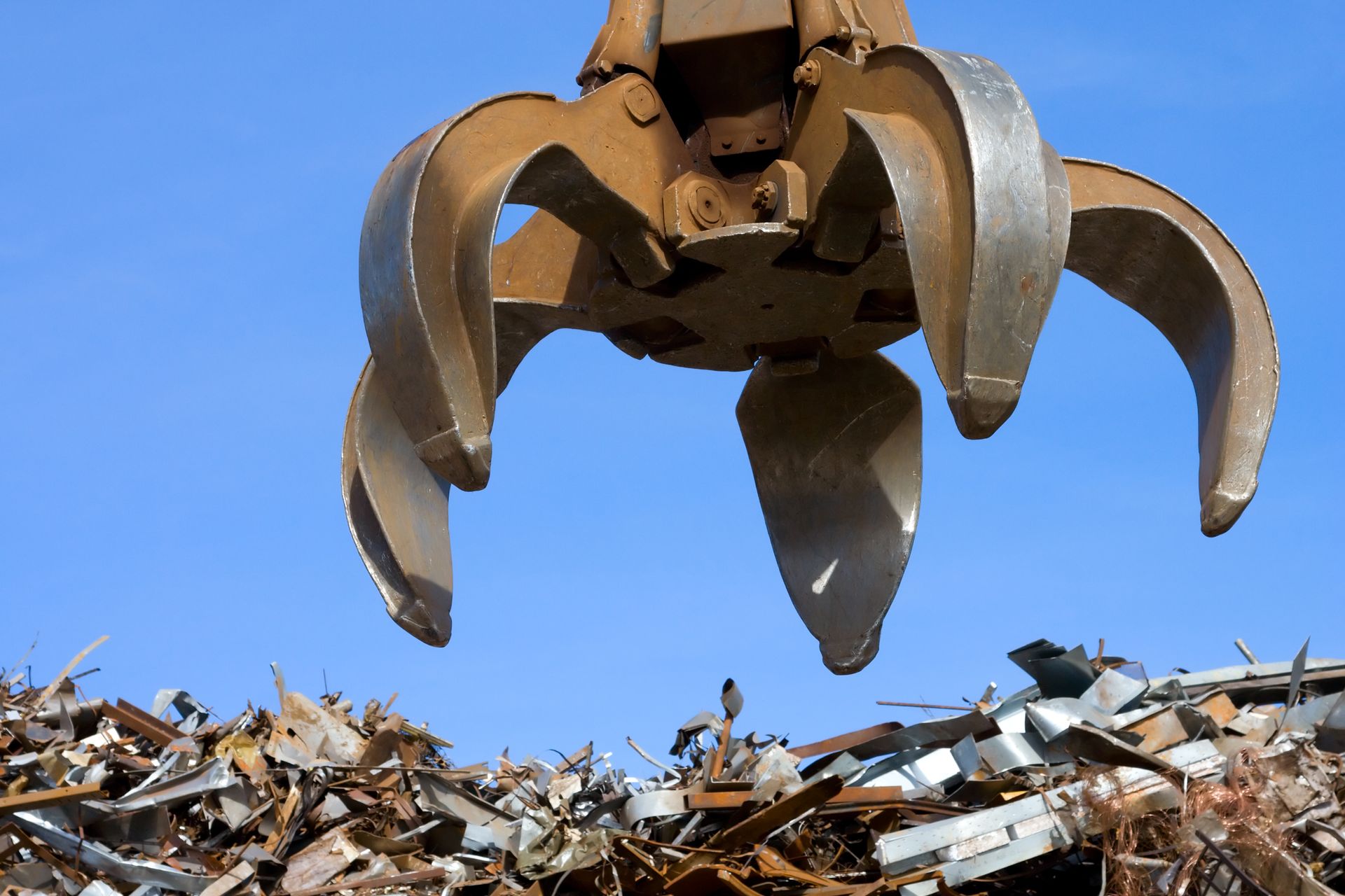 Una gru sta scavando in un mucchio di rottami metallici.