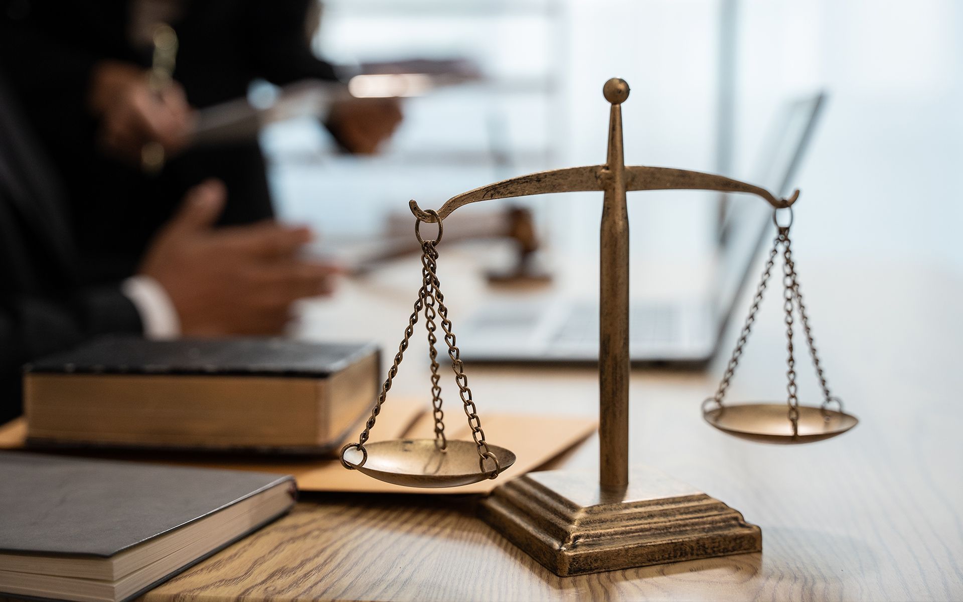 Scales of justice on a desk with law books and two people working in the background.