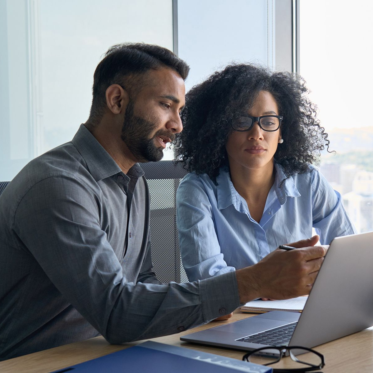 Man and woman looking at laptop, discussing data in a bright office setting.