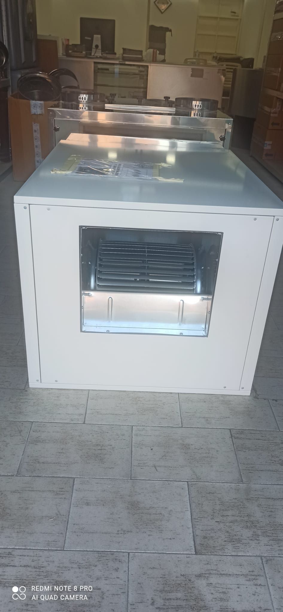 Elettrodomestico o mobile industriale bianco con ventilazione frontale, posizionato su un pavimento piastrellato in una stanza.