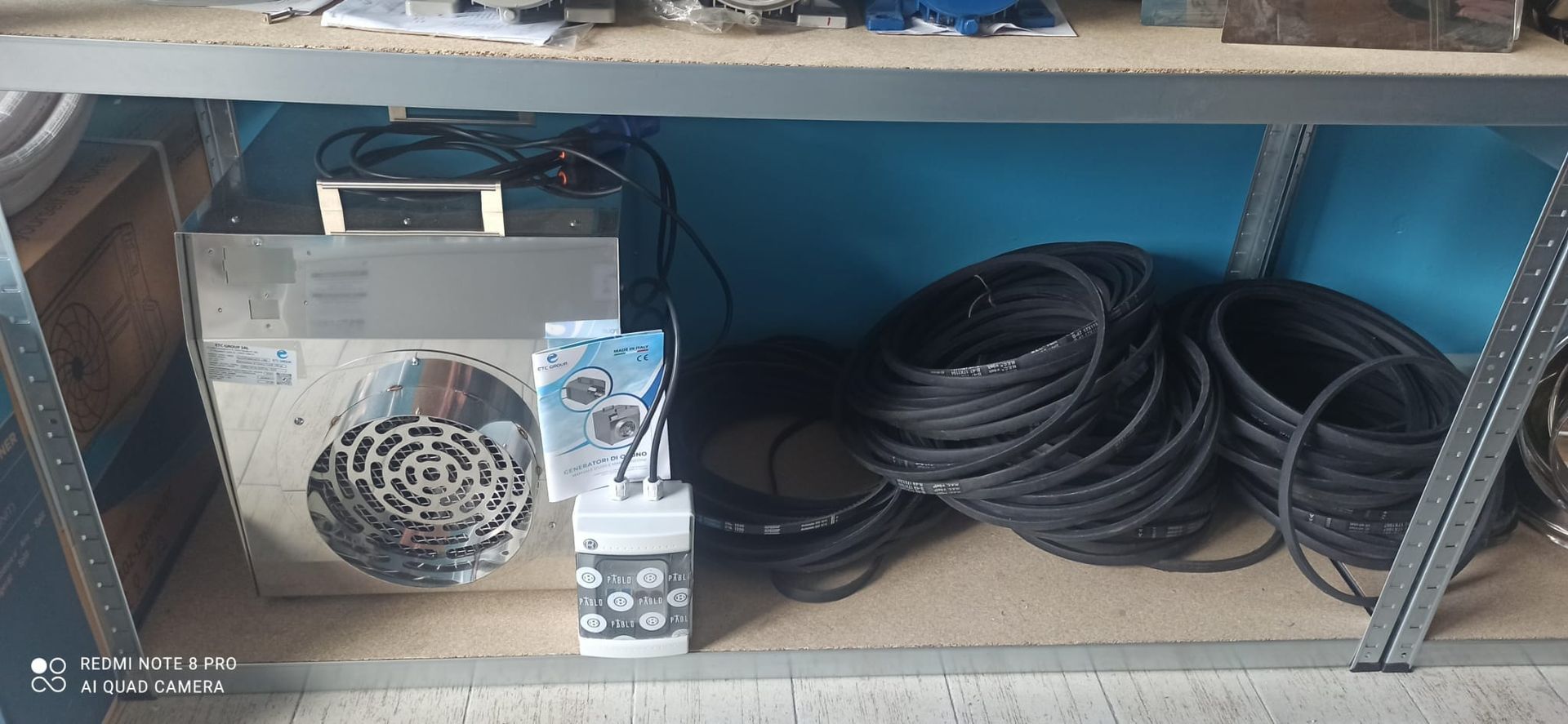 Macchina metallica con ventola e tubi neri arrotolati, riposta su uno scaffale impolverato in un'officina.