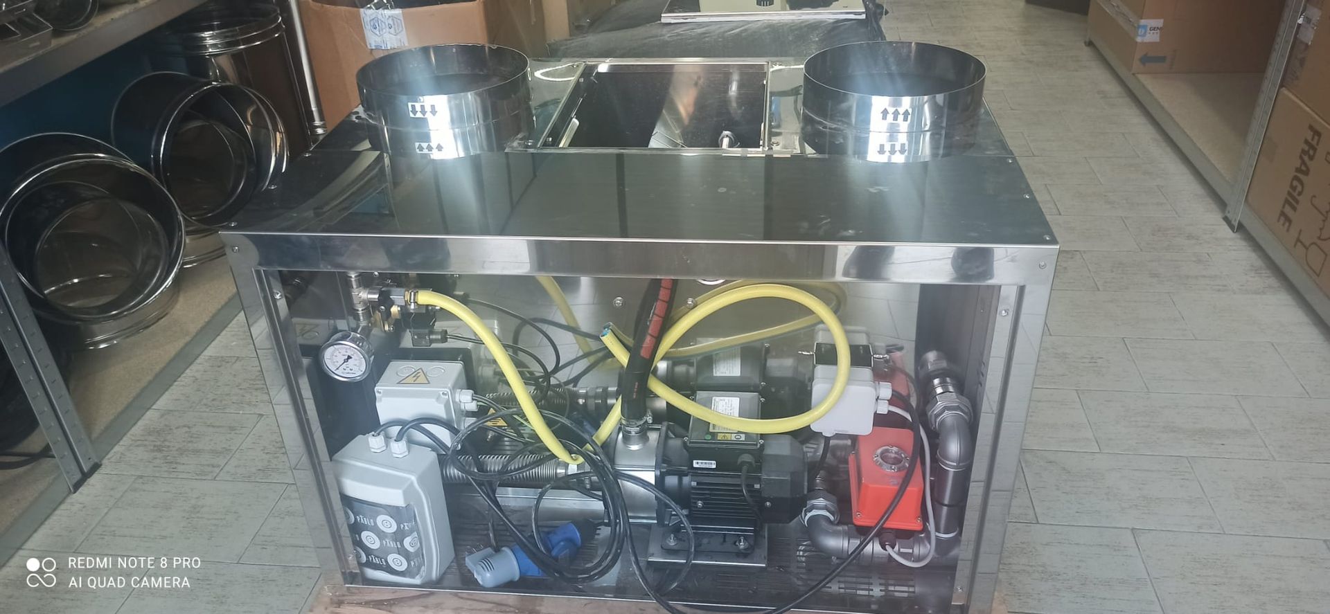 Carter metallico aperto con tubi, cablaggi e componenti gialli sul pavimento di un'officina.
