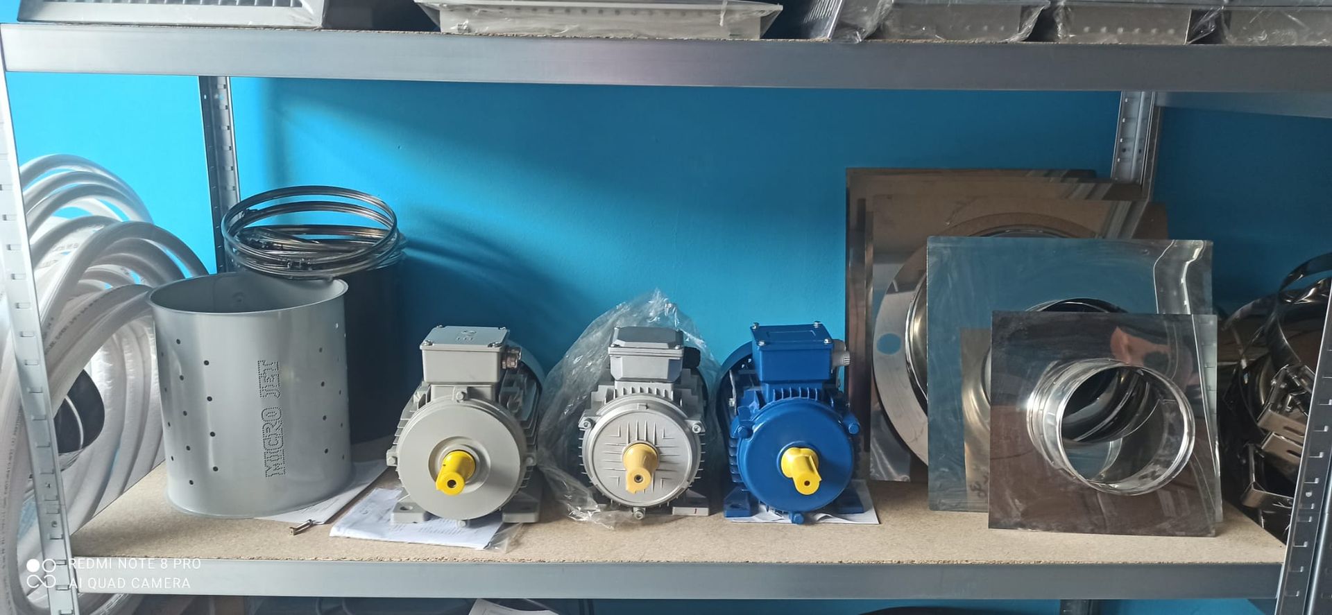 Componenti metallici di motori e condotti disposti su uno scaffale contro una parete blu.