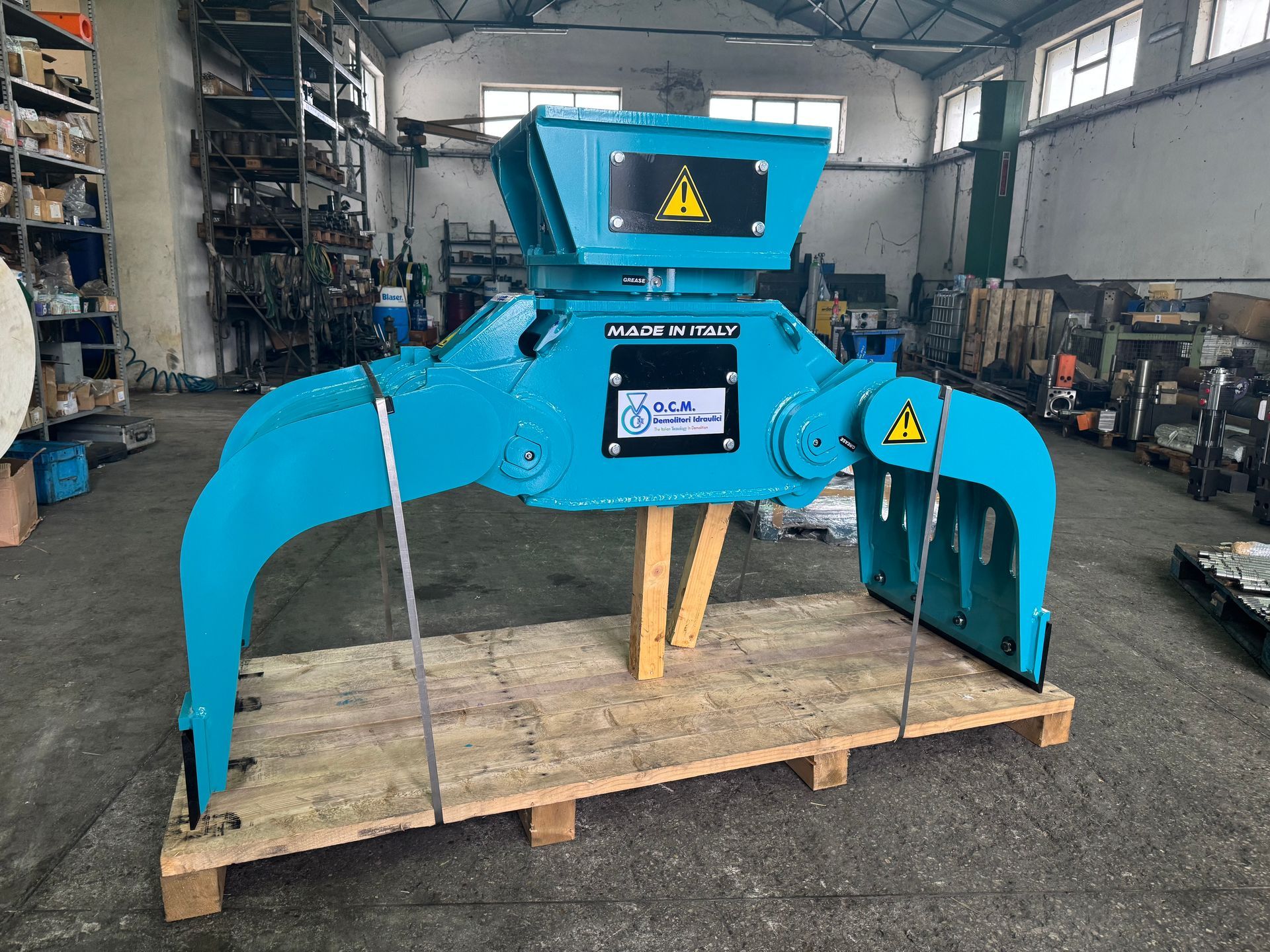 Attacco per pinza industriale blu su pallet di legno, in un magazzino.