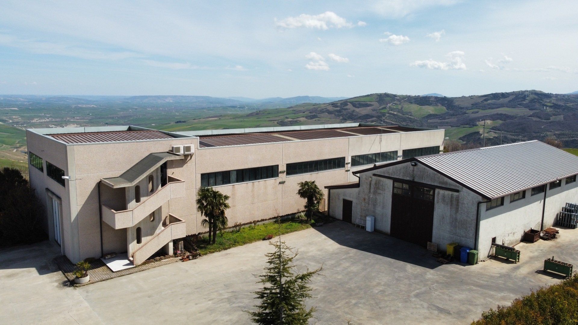 Edifici industriali su una collina, con un paesaggio circostante di dolci colline e un cielo azzurro.