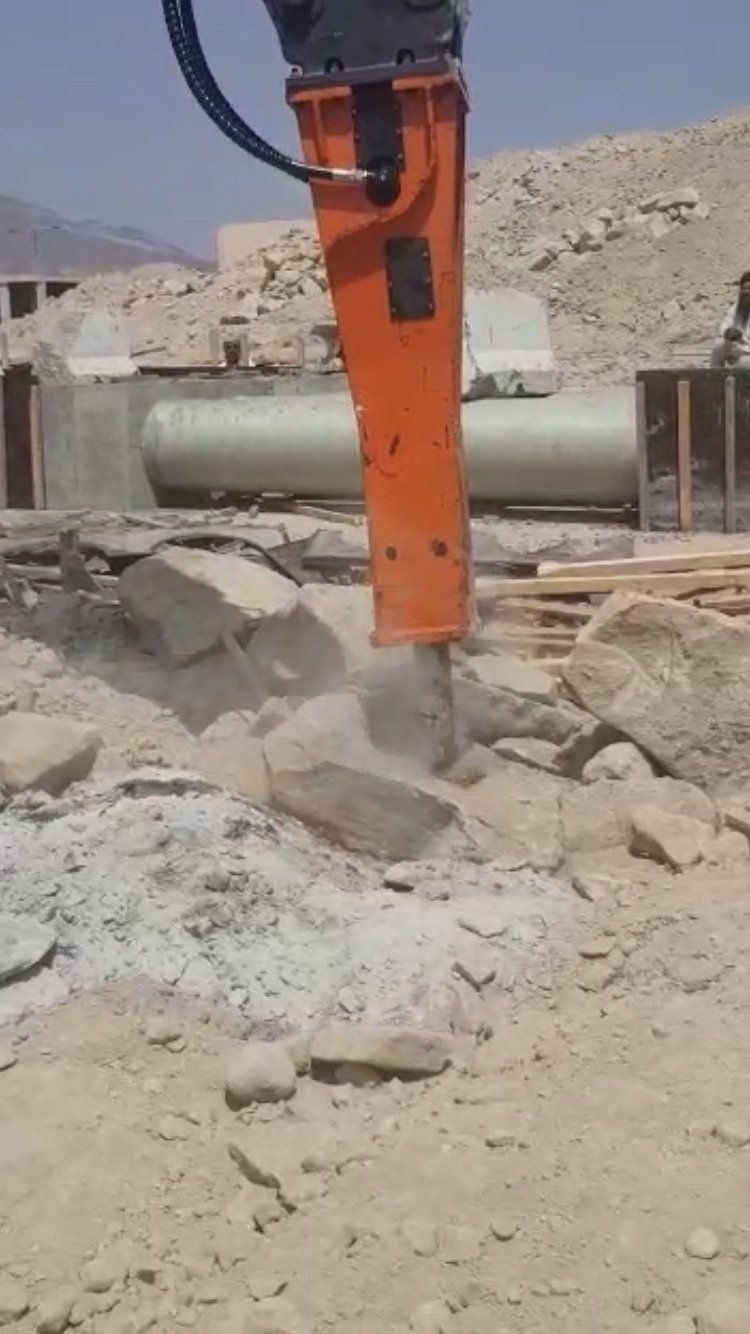 Un martello idraulico arancione che rompe le rocce in un cantiere edile.