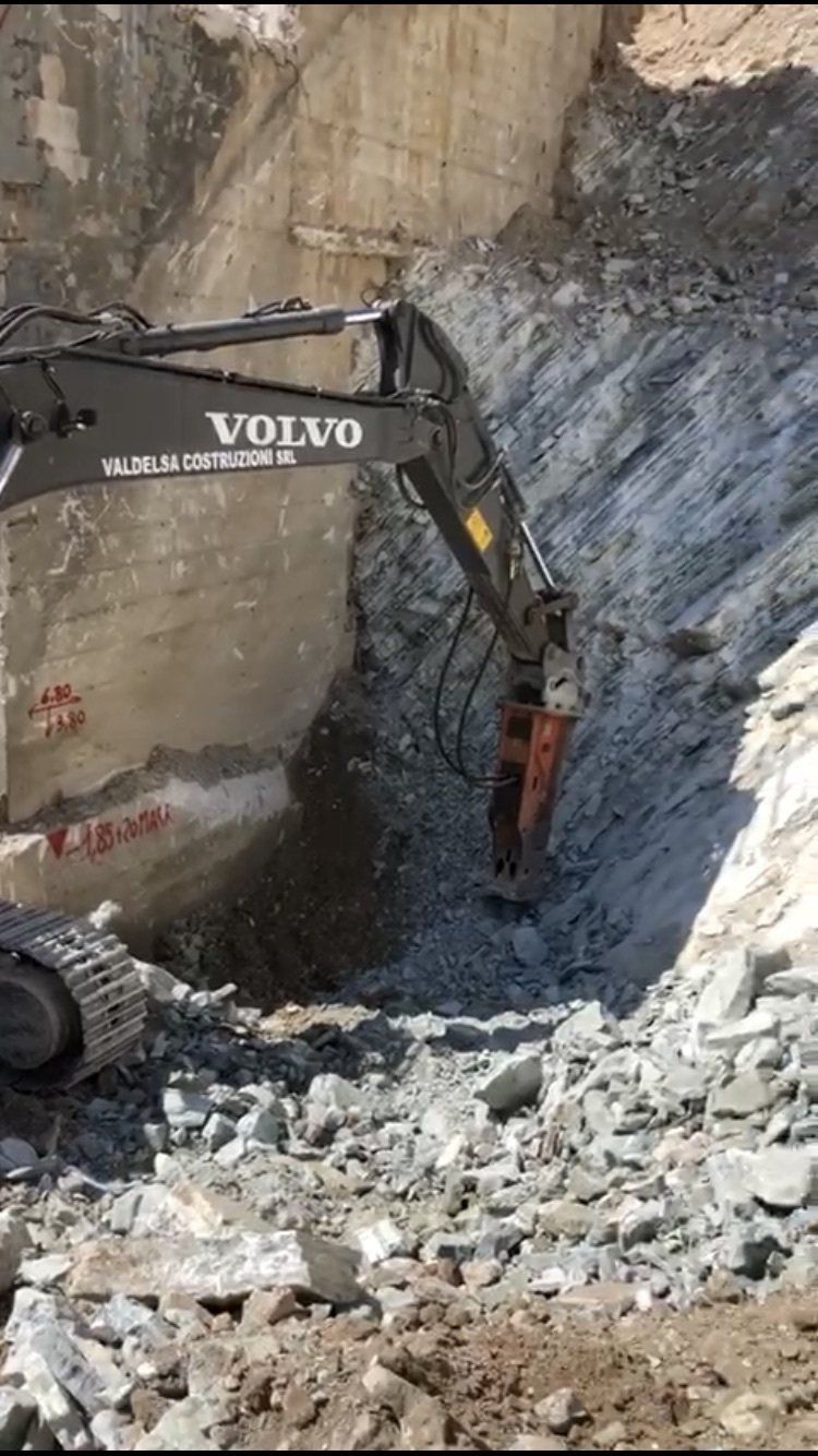 Un escavatore Volvo rompe una parete rocciosa in un cantiere edile.