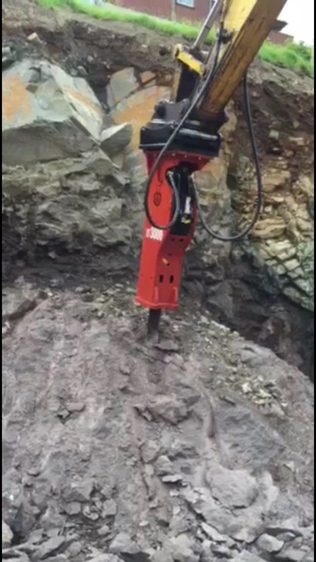Martello idraulico rosso che rompe la roccia in un cantiere edile.