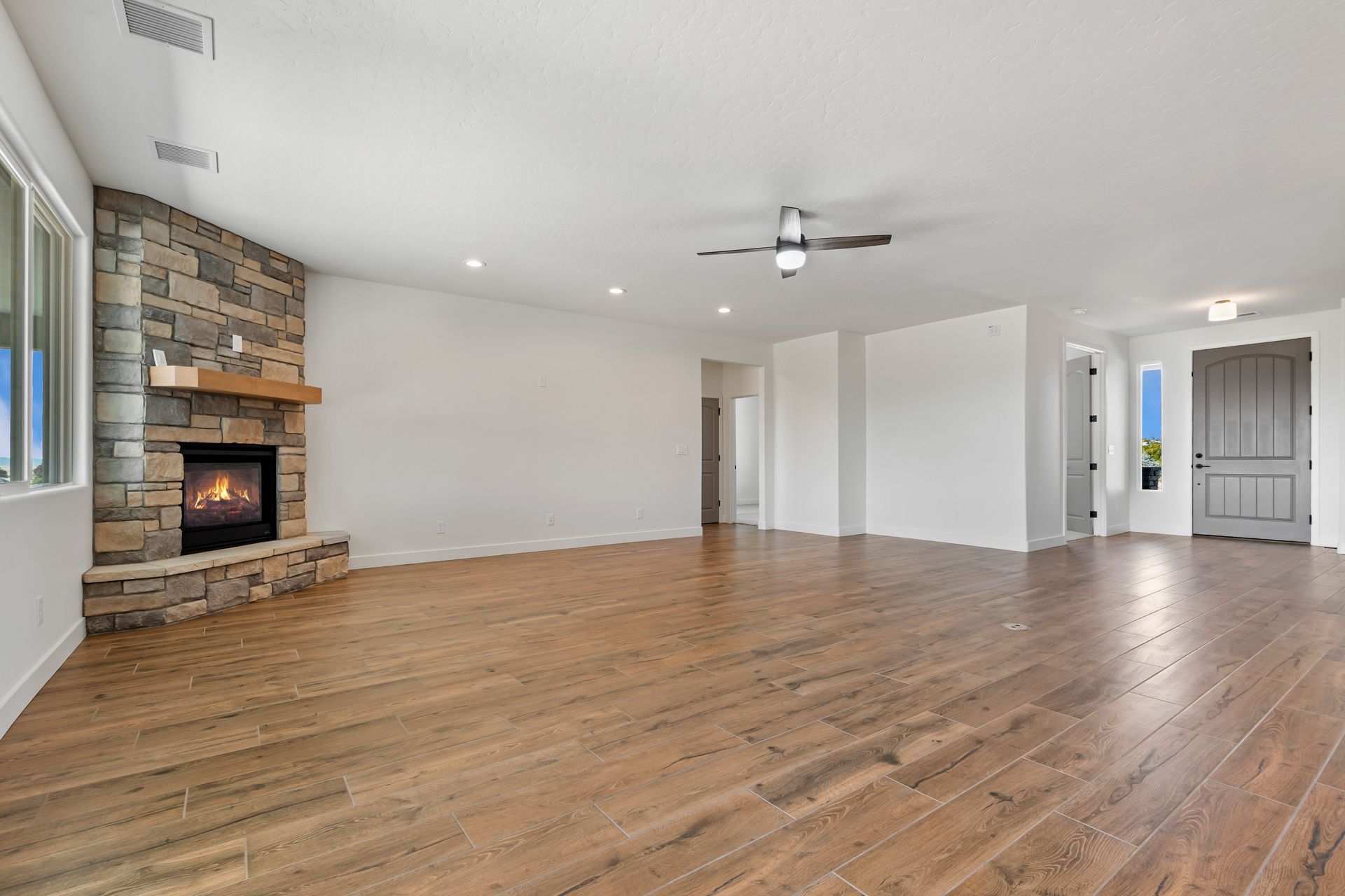 Empty living room with hardwood floors, stone fireplace, ceiling fan, and bright white walls Empty living room with hardwood floors, stone fireplace, ceiling fan, and bright white walls