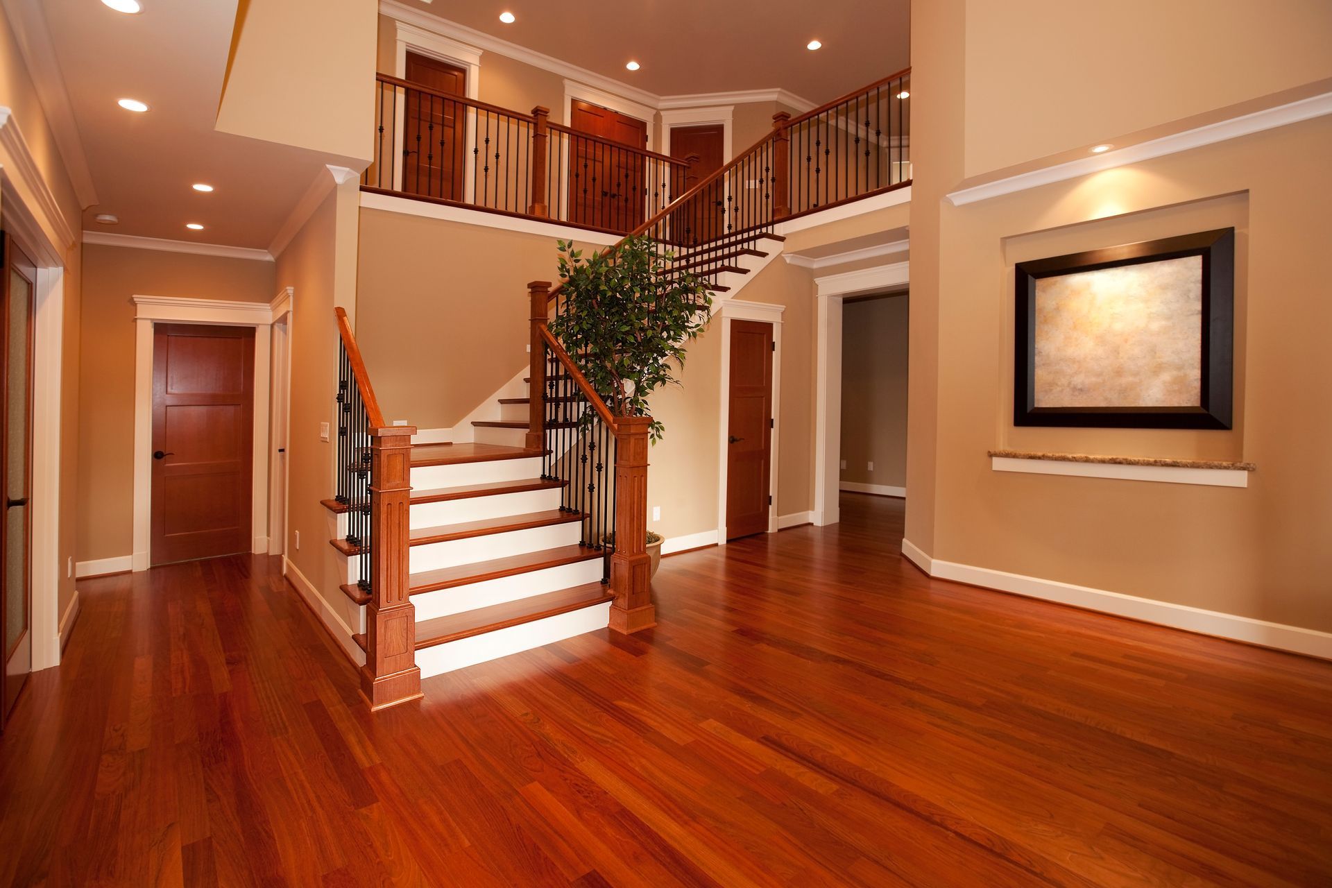 Warm-toned foyer with wooden floors, staircase, balcony railing, and framed wall art Warm-toned foyer with wooden floors, staircase, balcony railing, and framed wall art