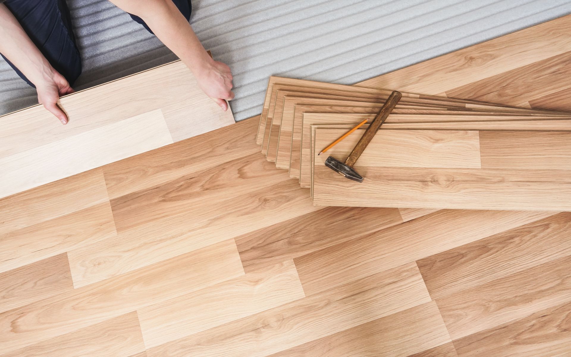 Person installing wooden flooring with a hammer and stacked floor planks on a light wood floor Person installing wooden flooring with a hammer and stacked floor planks on a light wood floor