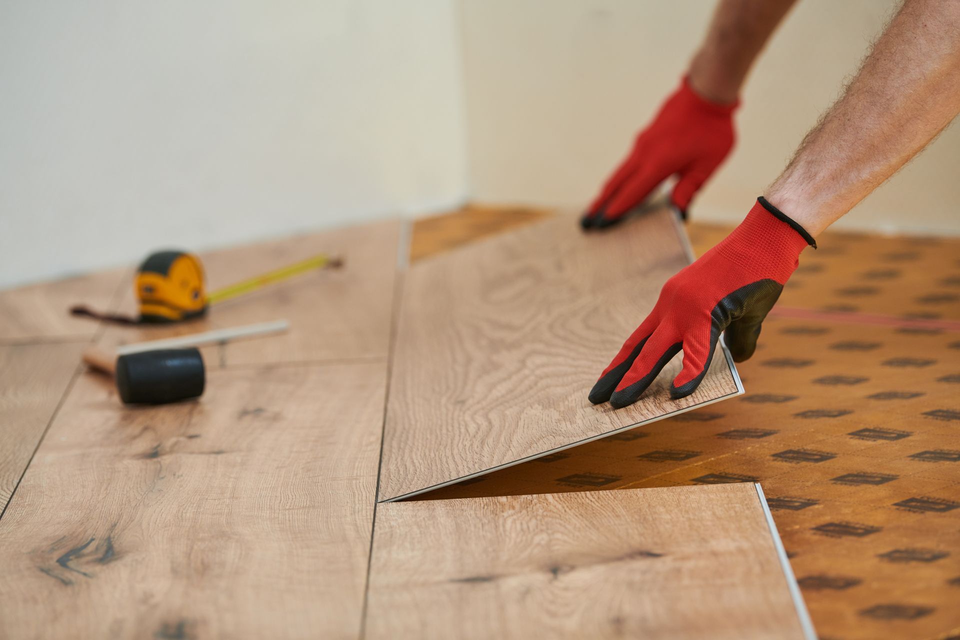 Gloved hands installing wood flooring with a saw and measuring tape nearby Gloved hands installing wood flooring with a saw and measuring tape nearby