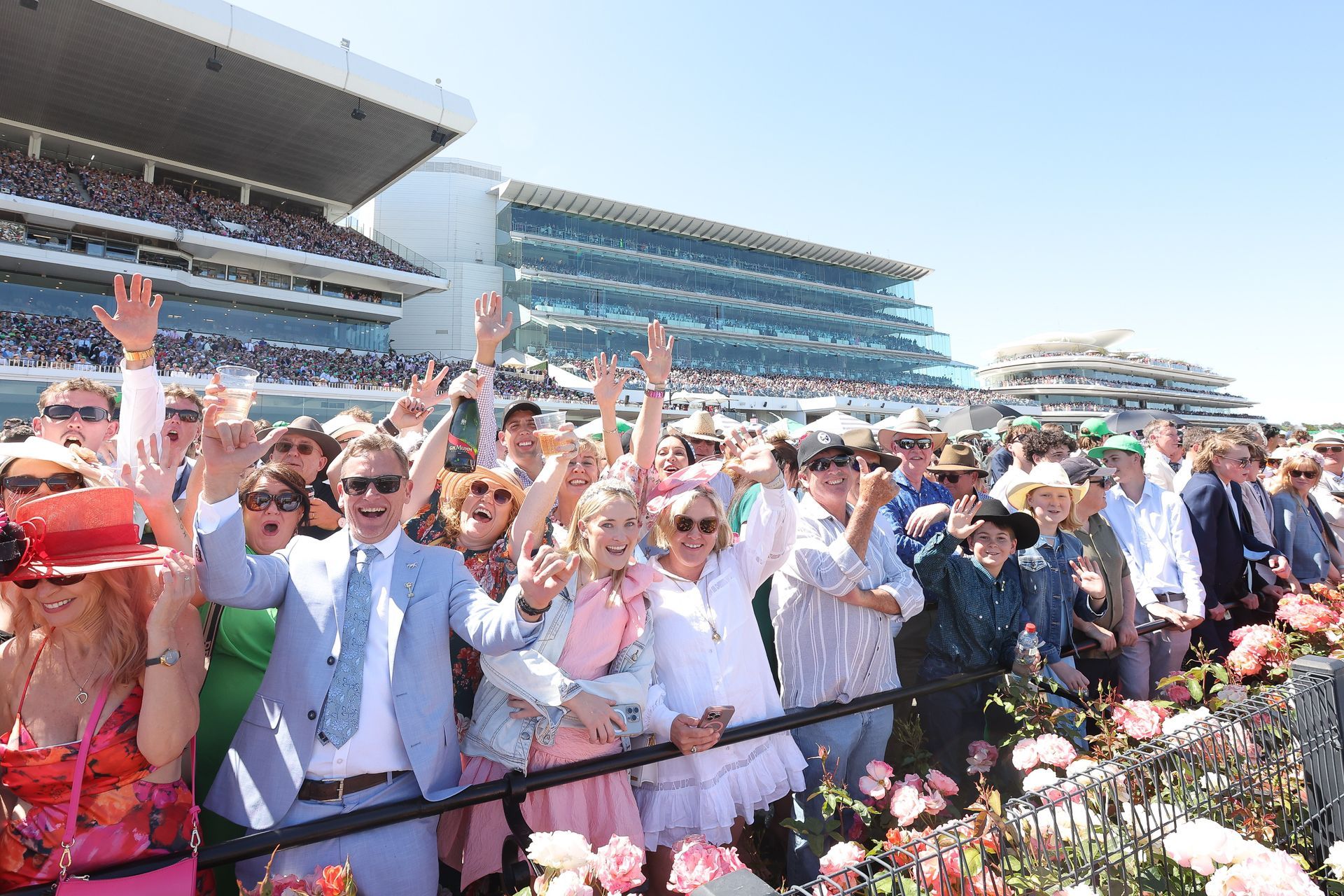 People at a racetrack waving with buildings and blue sky in the background.