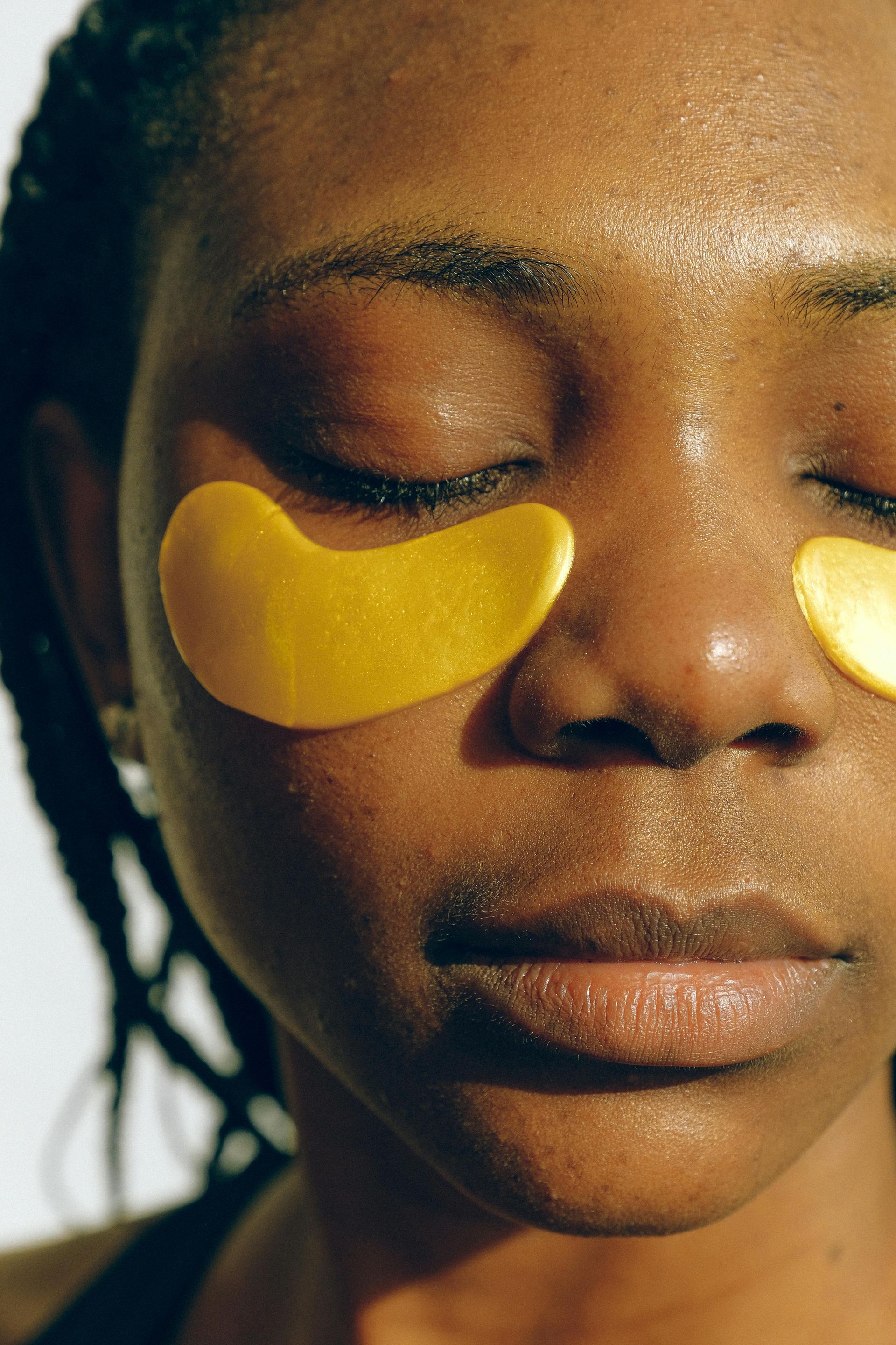 Close-up of person with closed eyes wearing gold under-eye patches on a white background.
