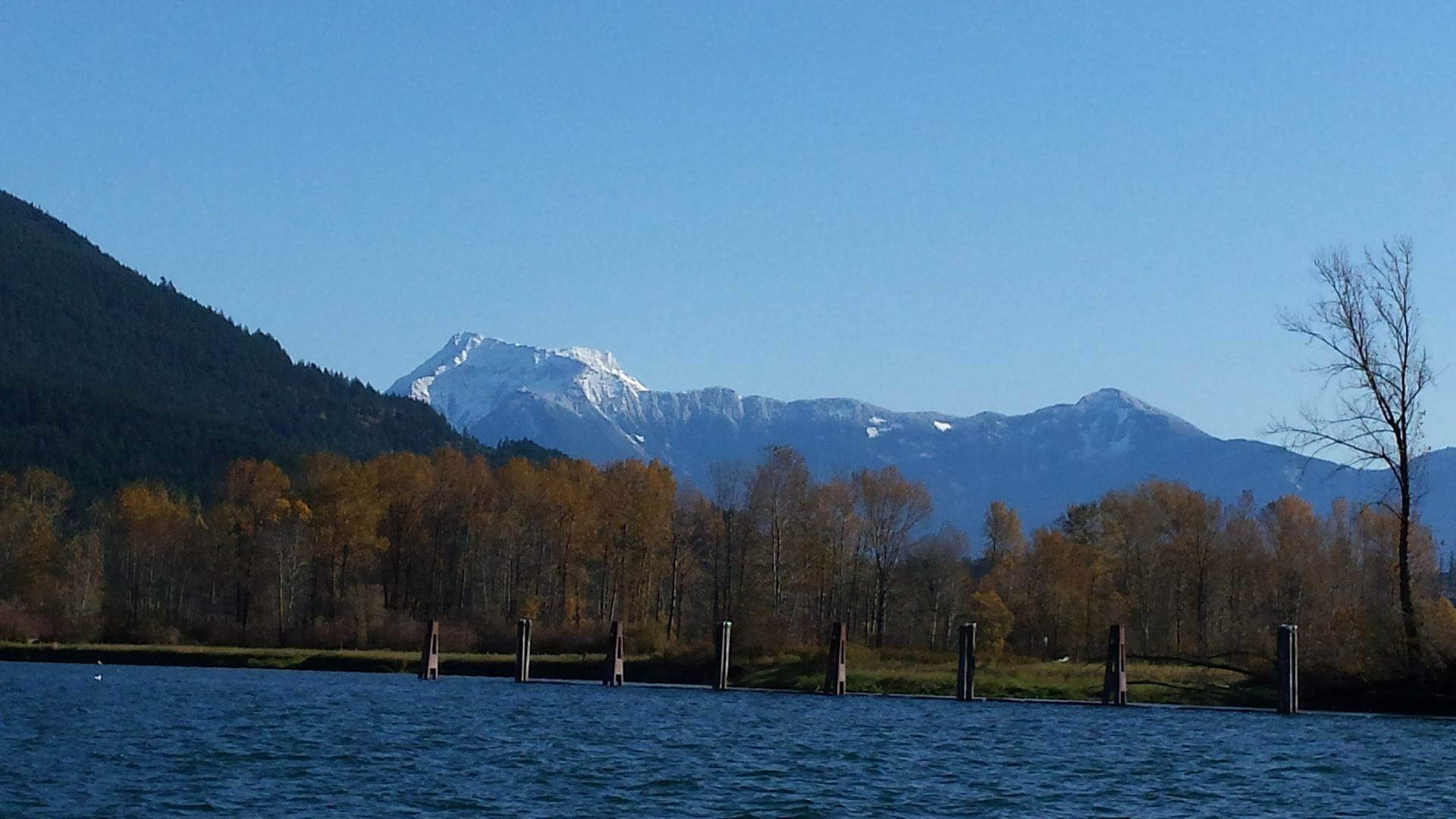 Snow-capped mountains beyond a blue lake and autumn trees under a clear sky