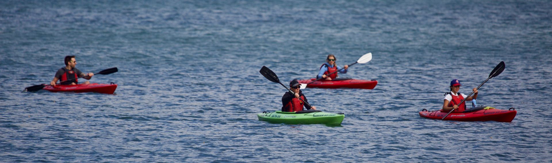 Three kayakers in red and green kayaks on open water, paddling in a calm sea.