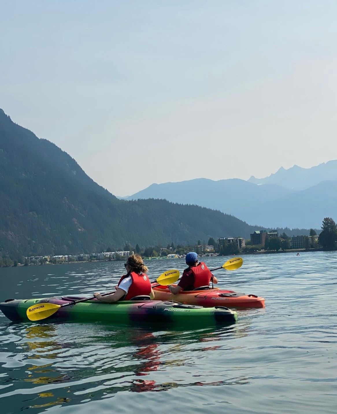 Two people kayaking on a lake with mountains in the background