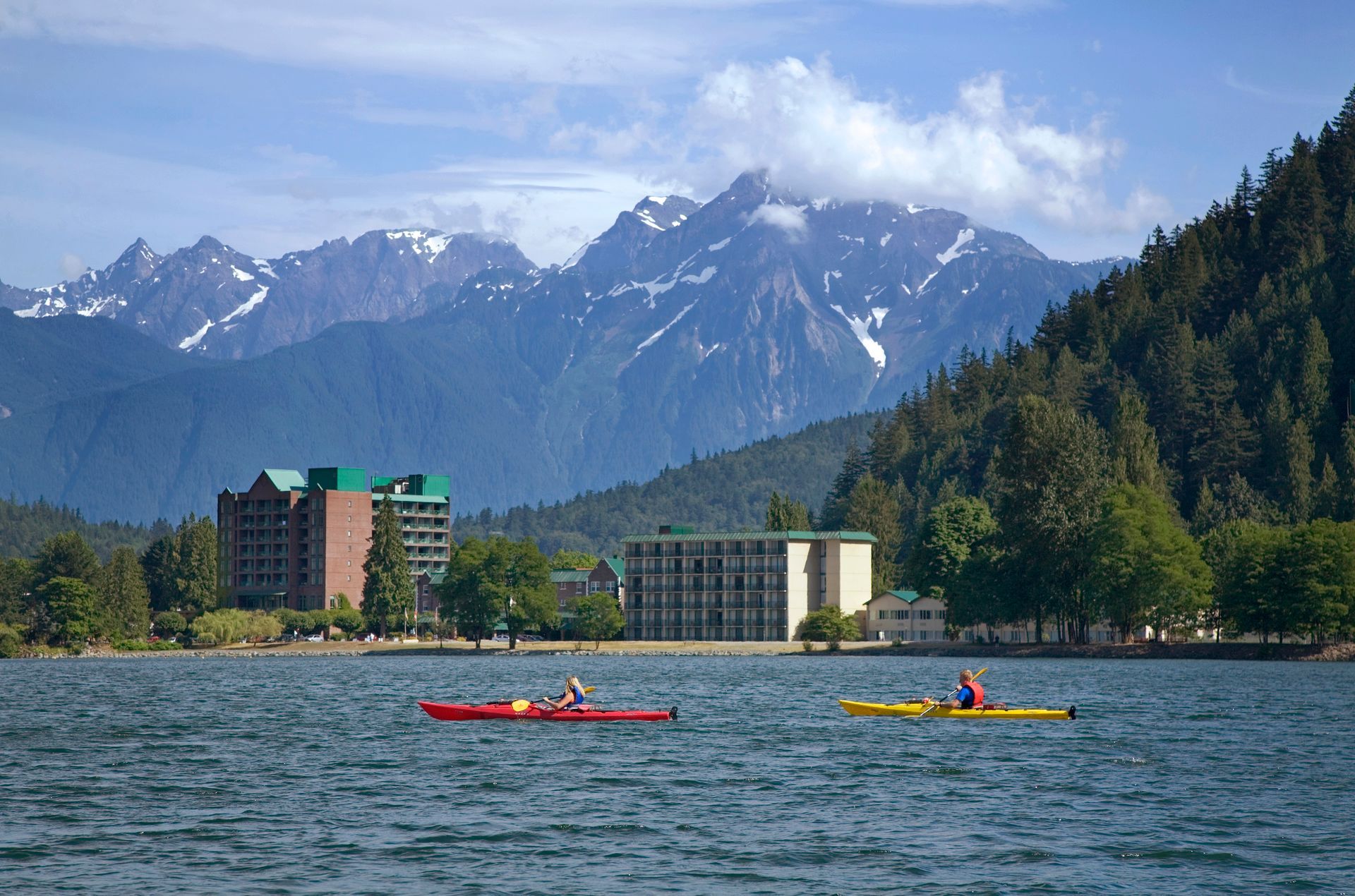 Two kayaks on a lake with mountains, forest, and buildings in the background