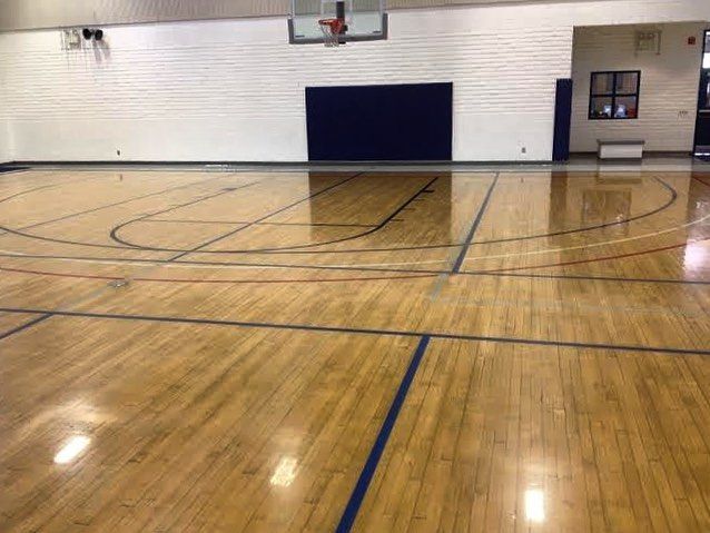 An empty gym with a wooden floor and a basketball hoop