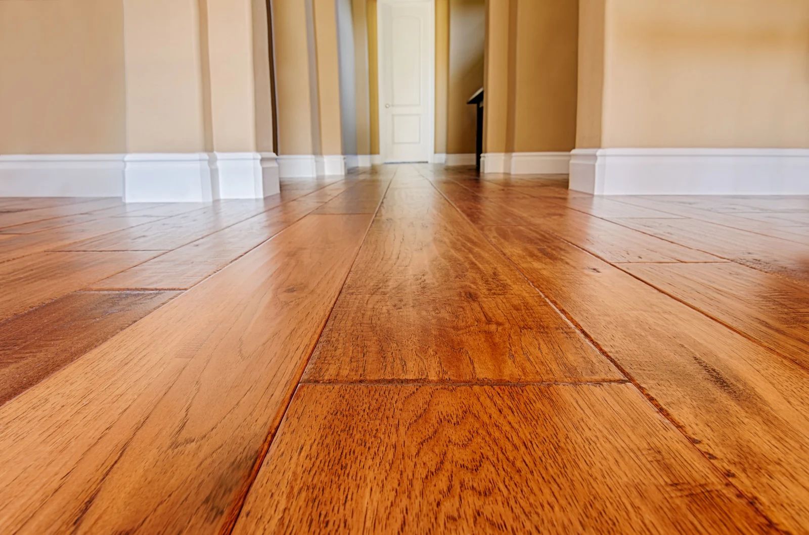 Polished wooden floor in a bright empty hallway with beige walls and white baseboards