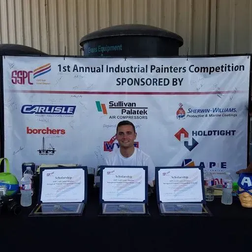 A man is standing in front of a sign that says 1st annual industrial painters competition