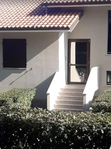 Vista frontale di una casa con tetto di tegole, scalini d'ingresso e cespugli davanti.