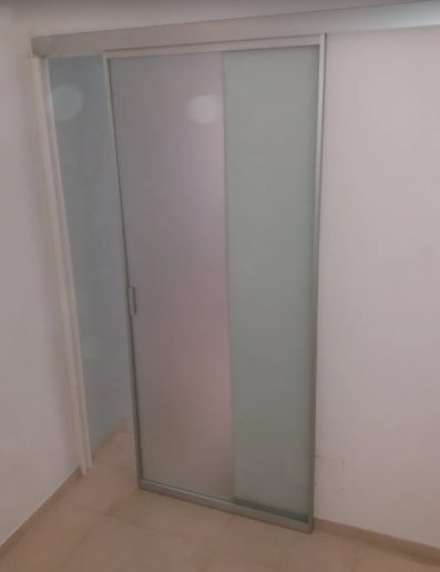 Porta scorrevole in vetro satinato con cornice grigia in una stanza bianca.