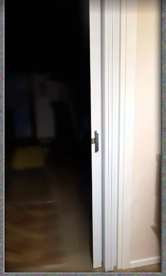 Porta bianca socchiusa che conduce a una stanza buia con pavimento in legno.