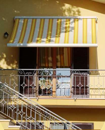 Balcone di un appartamento giallo con tenda da sole a righe e ringhiera in metallo bianco sopra una scala