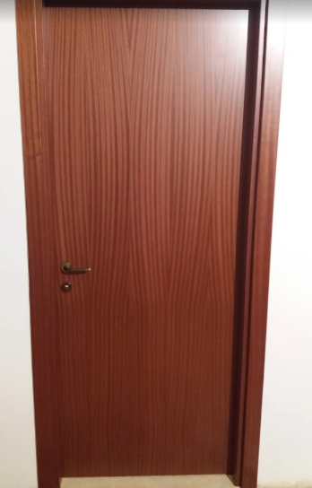 Porta chiusa in legno marrone con maniglia in metallo e cornice bianca a muro.