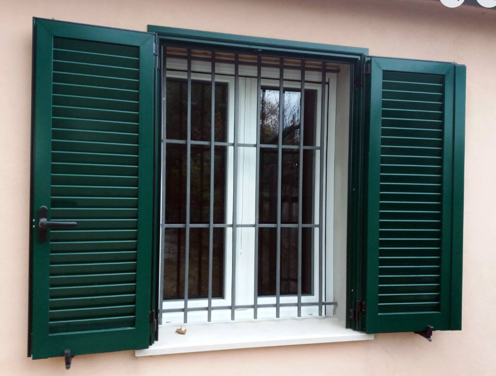 Finestra con persiane verdi e sbarre metalliche su una parete beige