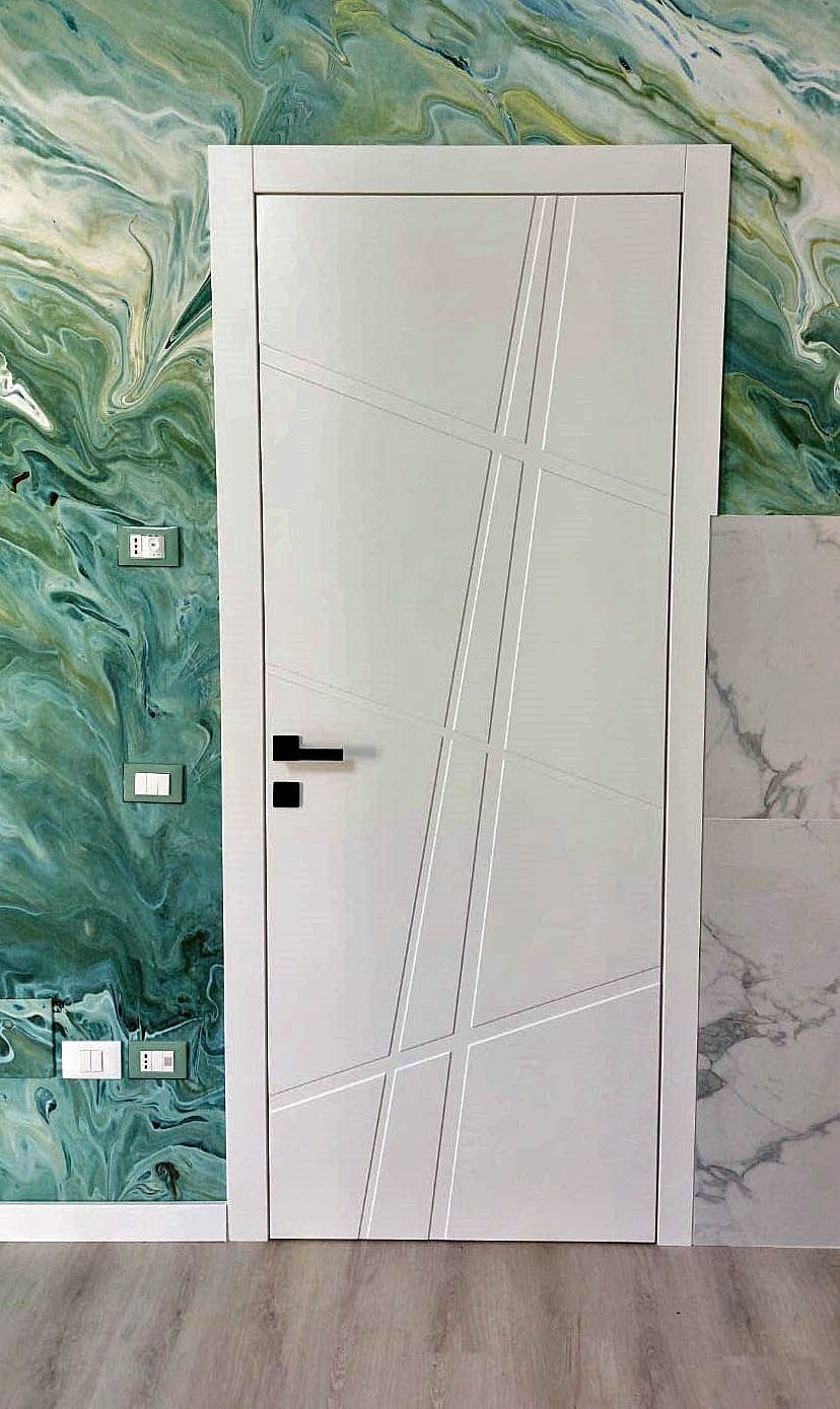 Porta interna a pannelli bianchi con maniglia e serratura argentate, mostrata in un corridoio.