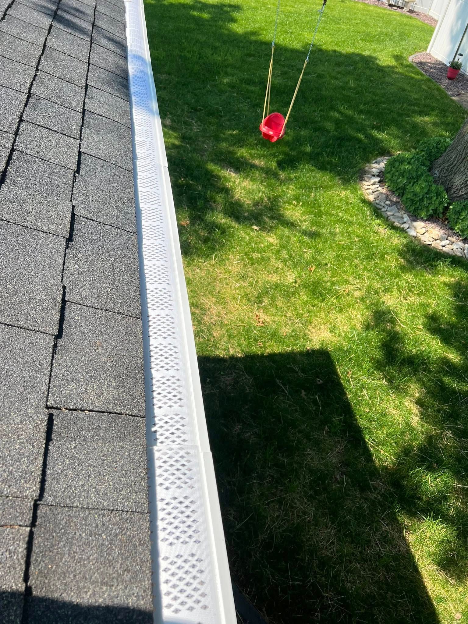 A view from a roof looking down at a white gutter guard and a small red swing hanging over a grassy lawn.