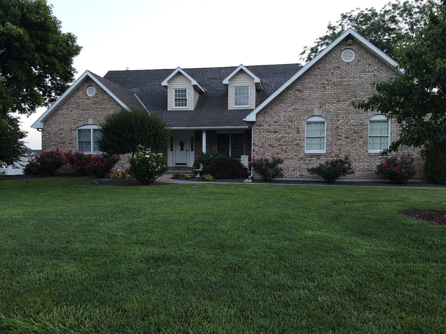 Single-story stone house with a front lawn and dormer windows under an overcast sky