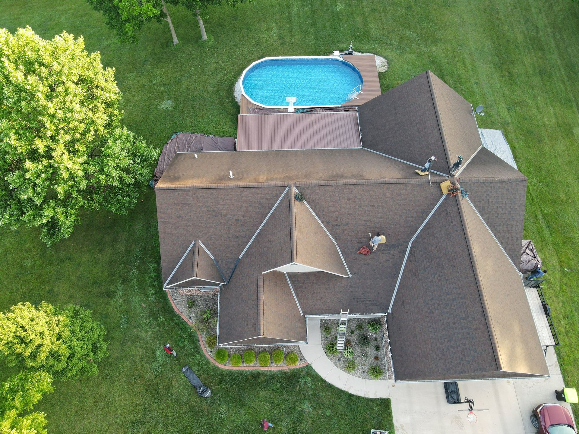 Aerial view of a house with a backyard pool, surrounded by green lawn and trees.