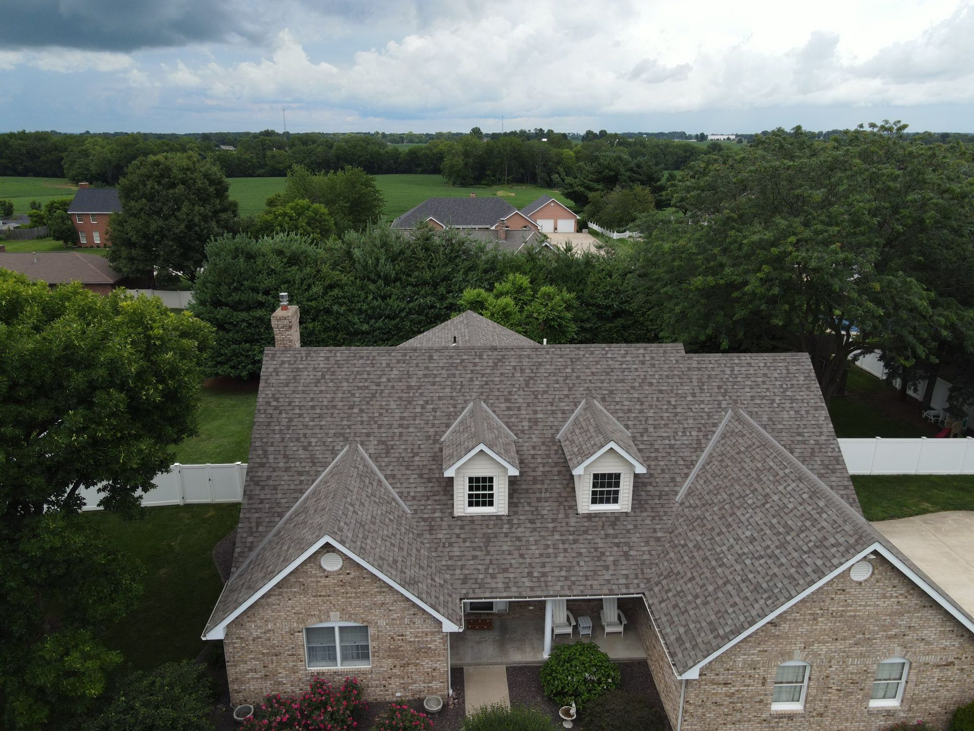 Aerial view of a suburban house with a gray roof, surrounded by trees under a cloudy sky