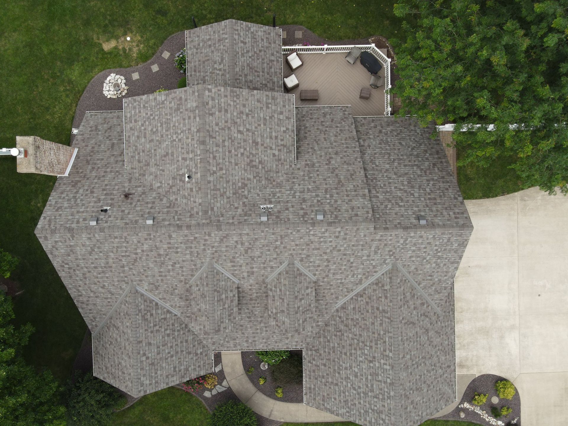 Aerial view of a gray-shingled house roof surrounded by trees and a driveway.