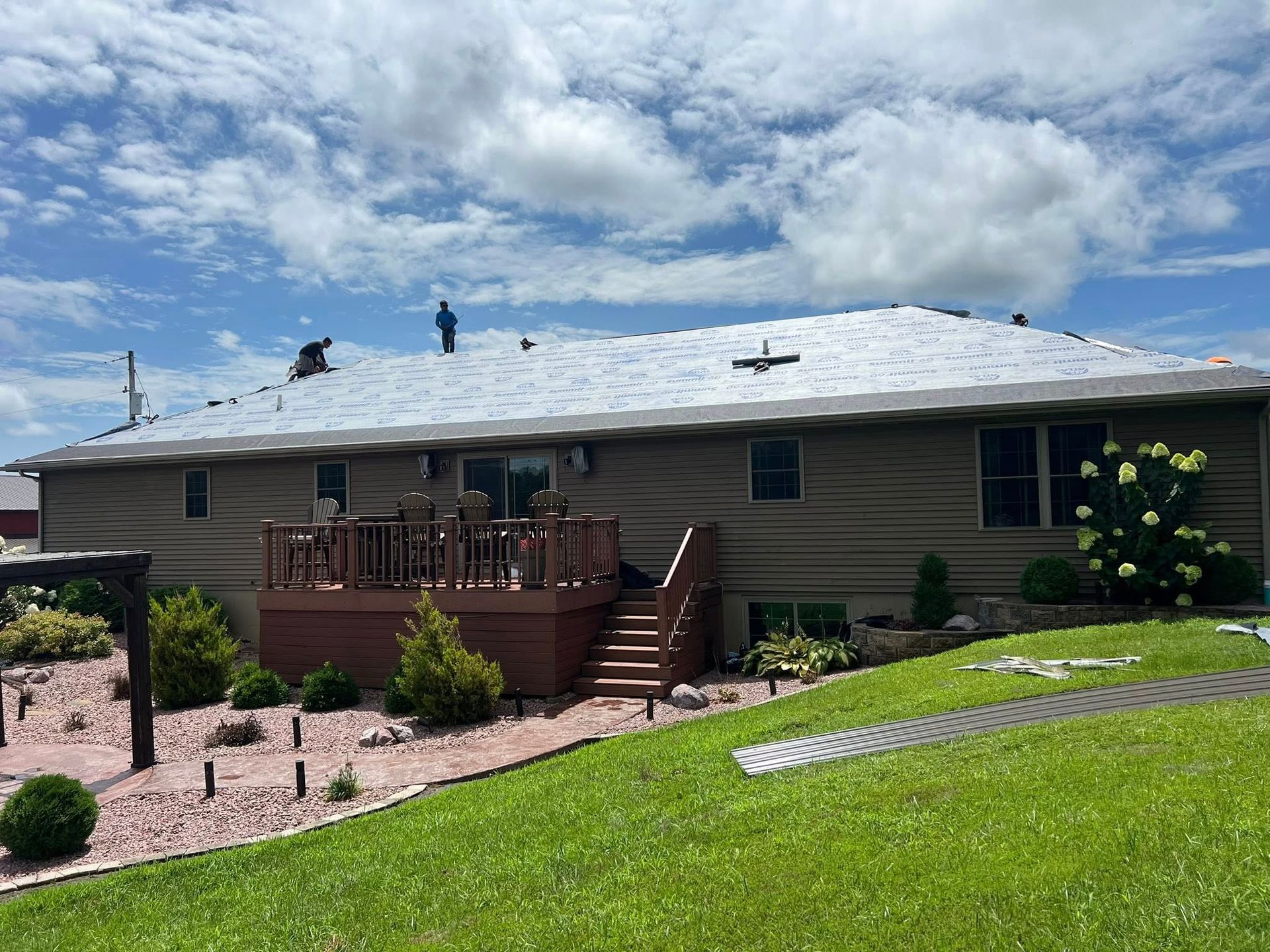 Suburban house with a deck and stairs, light siding, green lawn, and cloudy sky