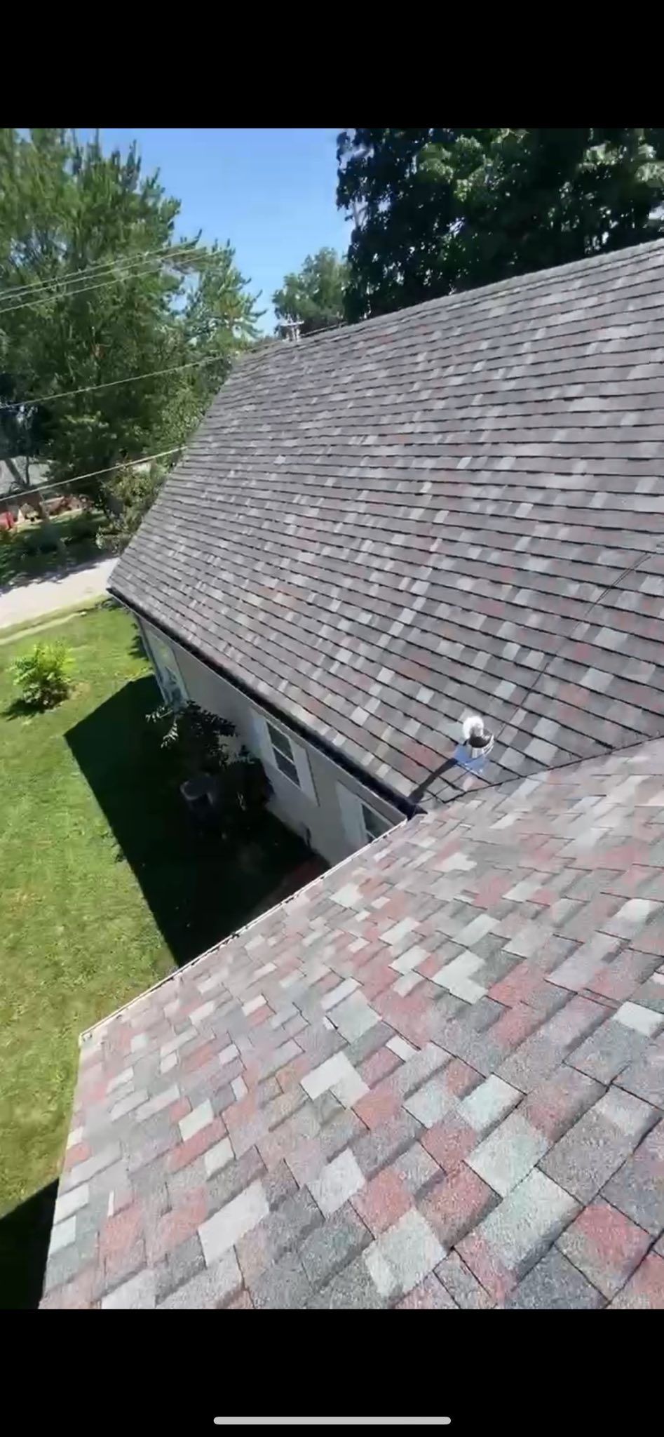 Shingled roof with a steep slope beside green trees and grass on a sunny day