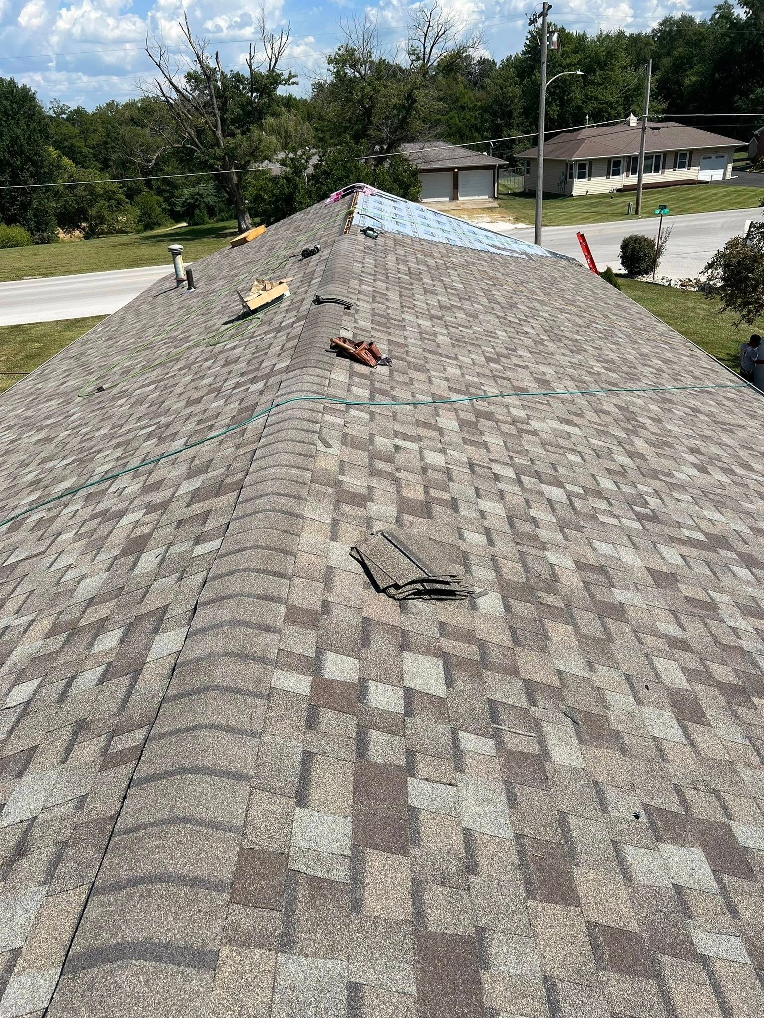 Roof covered with gray shingles and scattered debris after storm damage, viewed from above