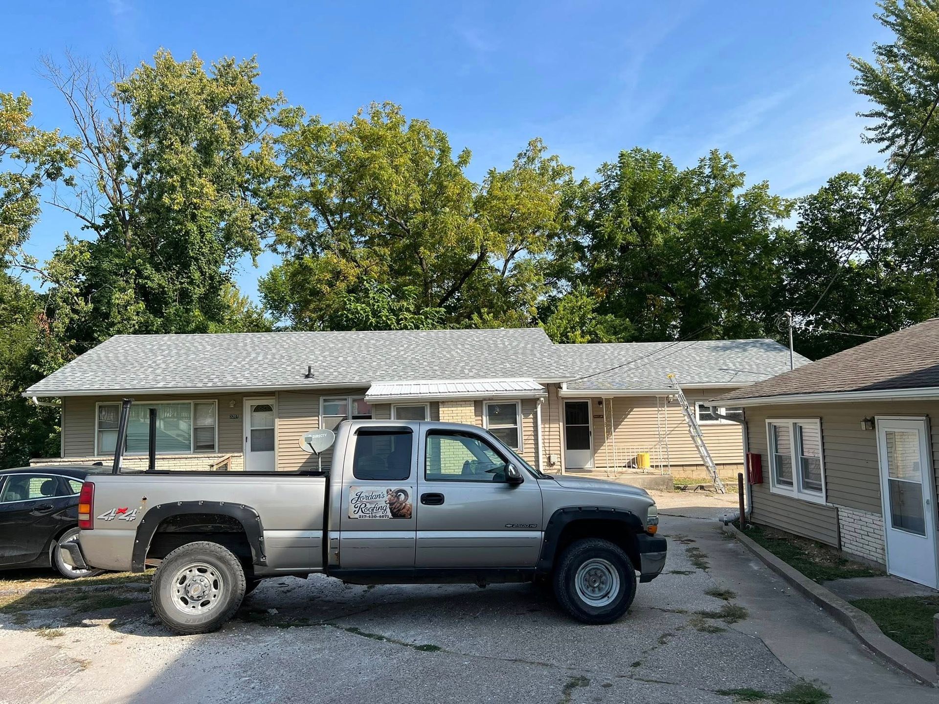 Two-tone pickup truck parked in a driveway beside a single-story house under a blue sky
