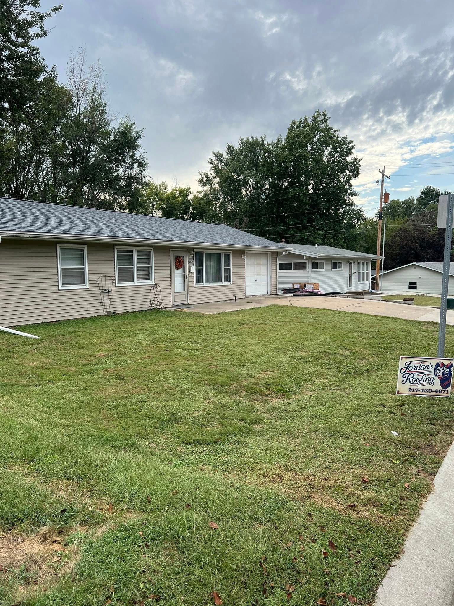 Single-story beige house with a front lawn, driveway, and overcast sky.