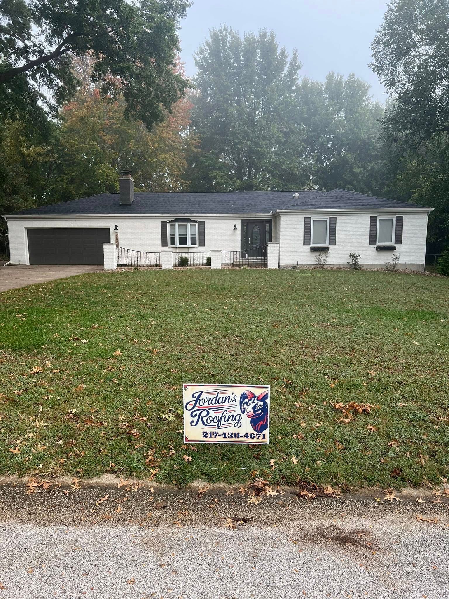 White ranch house with garage, leaf-covered lawn, and a small sign in front.