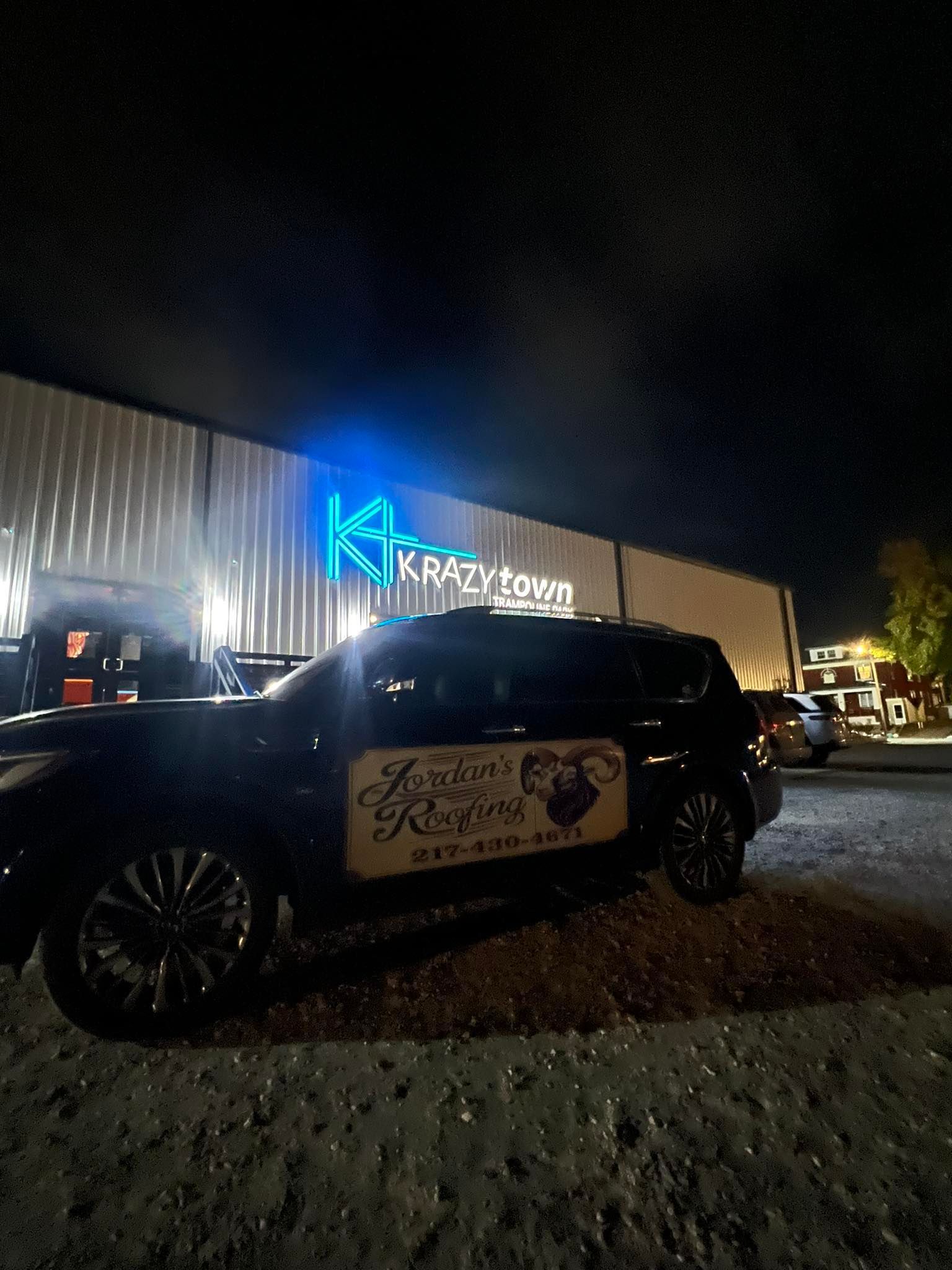 Nighttime parking lot with a black SUV in front of a lit building sign.
