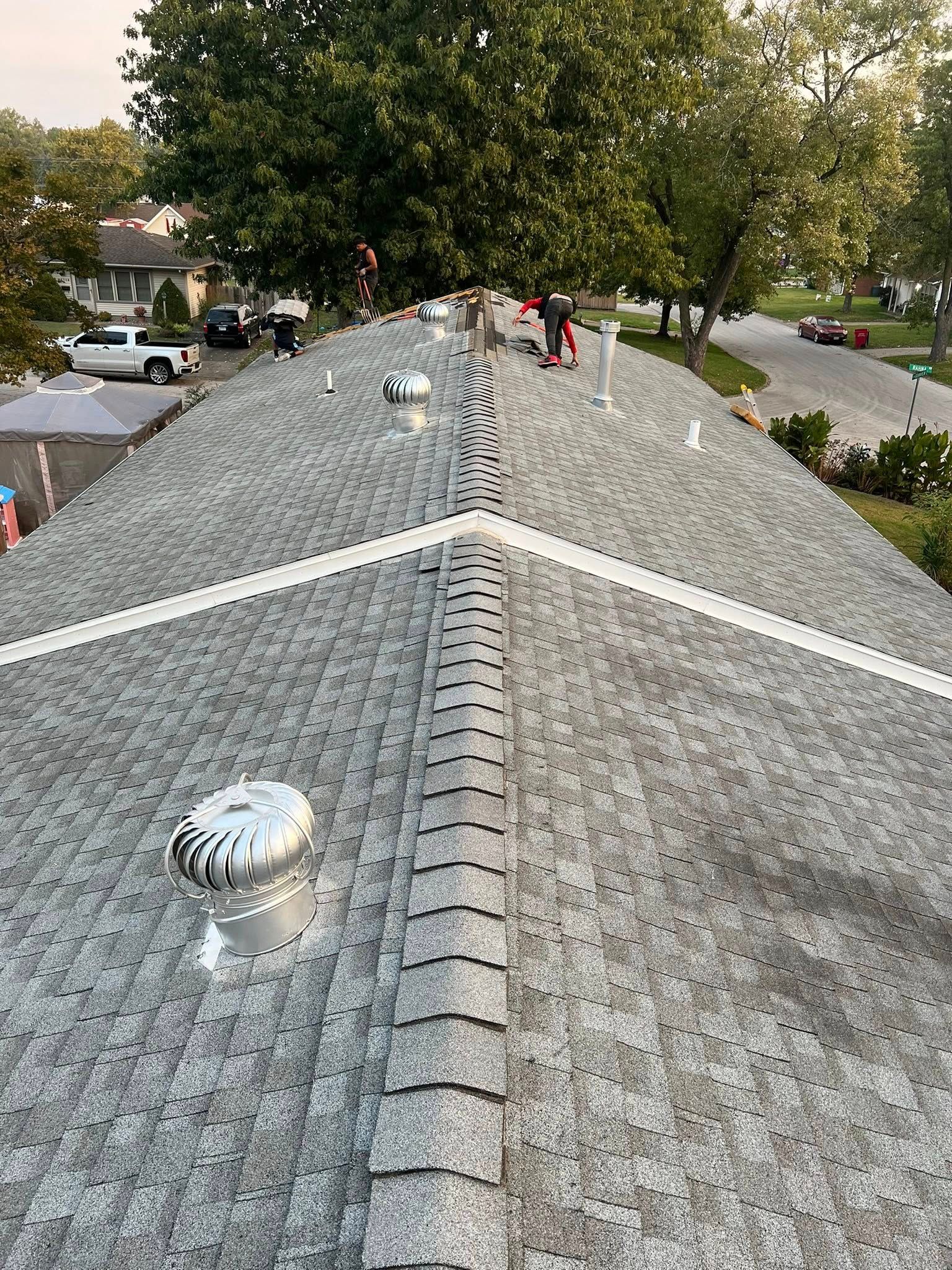 Roof shingles with two metal vents, viewed from the ridge over a tree-lined neighborhood street.