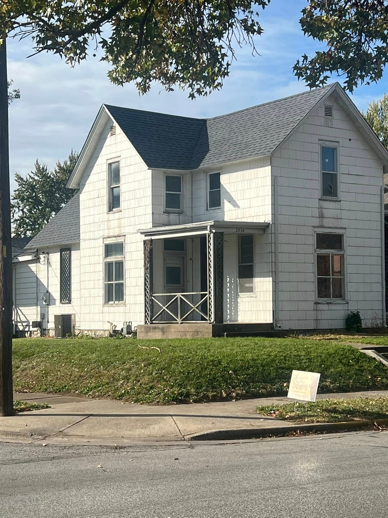 Two-story white house with gray roof and a small front porch on a tree-lined street