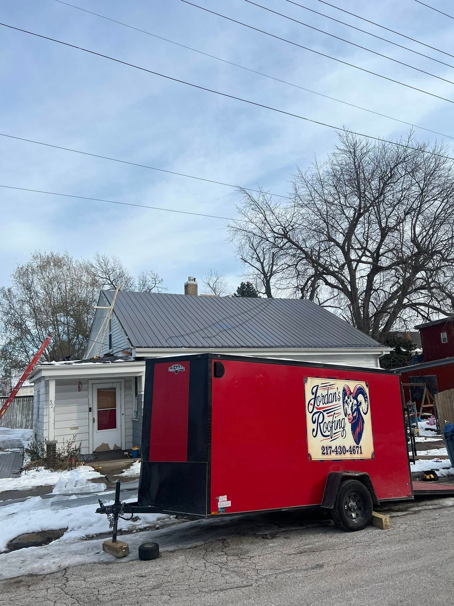 Red food trailer parked in snowy yard beside a house, with a beige menu sign and bare trees.