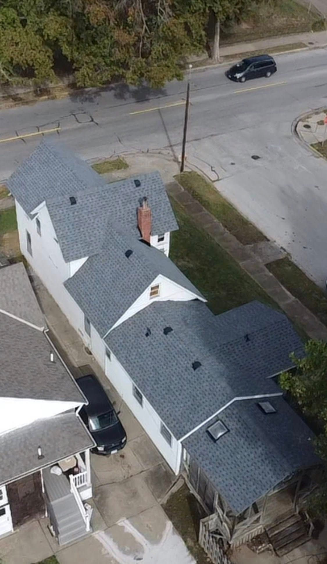 Aerial view of a white house with gray roof beside a street and parked black car.